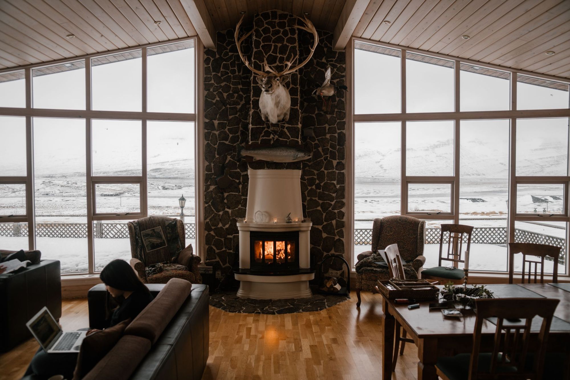 A warm living room with a fireplace and snowy mountains outside the windows